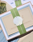 Seashell-themed wedding invitation with green ribbon and envelope.