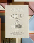 Wedding invitation card with 'carolina gomez & timothy hughes' text, surrounded by other stationery items.