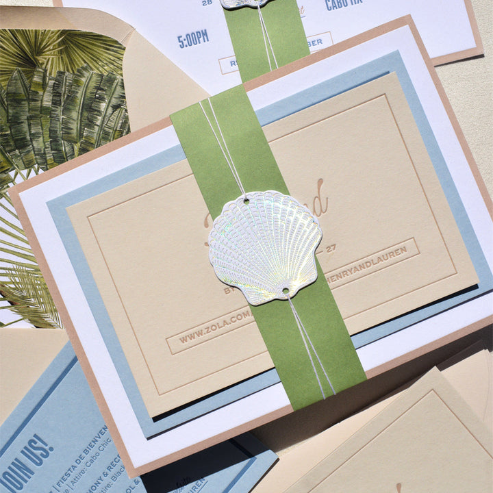 Seashell-themed wedding invitation with green ribbon and envelope.