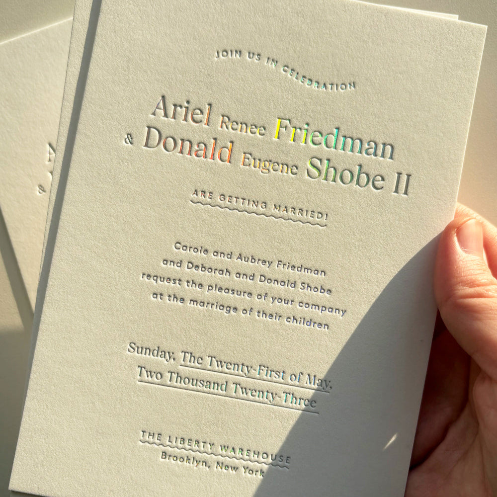 Wedding invitation card held by a hand with a neutral background