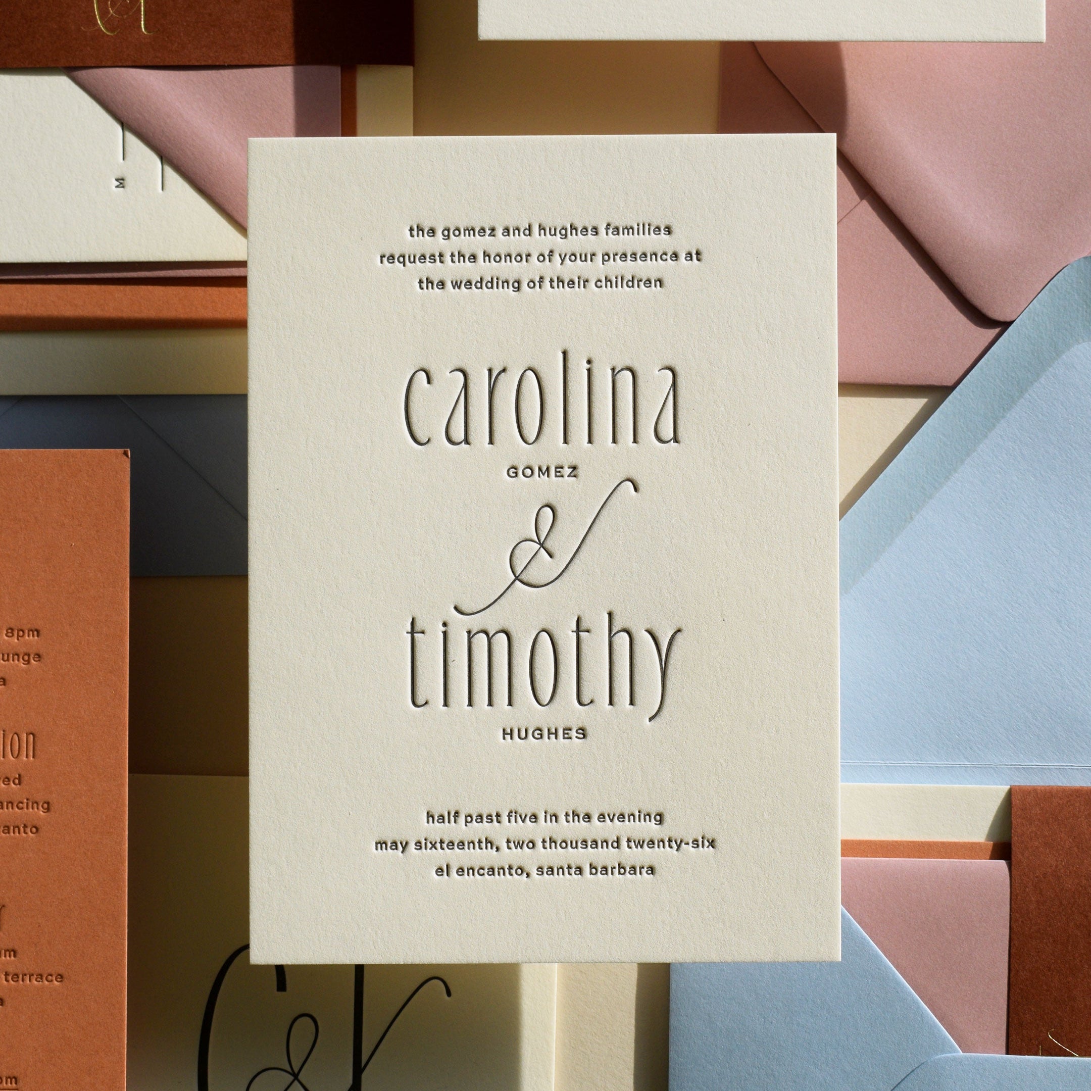 Wedding invitation card with 'carolina gomez & timothy hughes' text, surrounded by other stationery items.